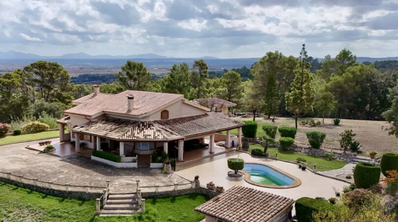 Luftaufnahme einer mediterranen Finca in Campanet mit Pool, Gartenanlage und Bergpanorama.