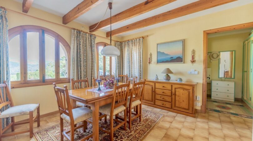 Helles Esszimmer der Finca in Campanet mit Holzbalken, rustikalem Esstisch und Blick ins Grüne.