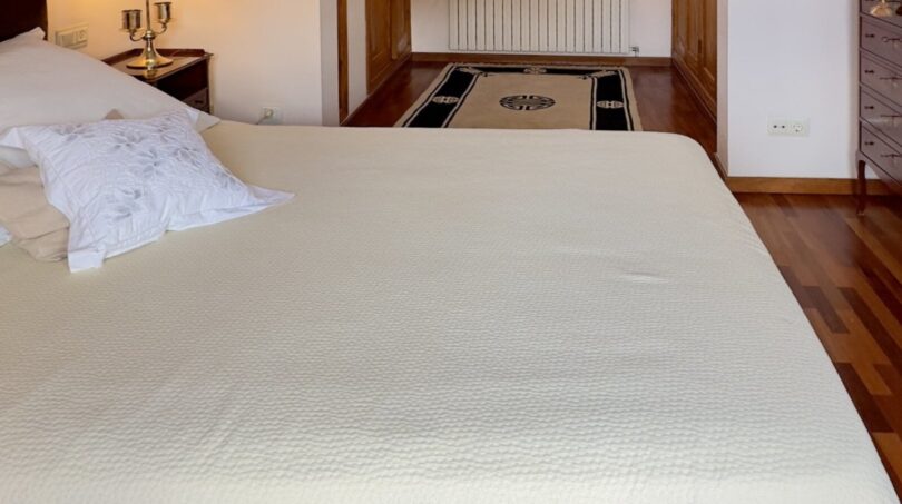Dormitorio luminoso con cama doble blanca, suelo de madera y elegante arco redondeado hacia el vestidor