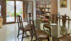 Elegante comedor con mesa de cristal, sillas de madera, lámpara de araña y estantería, con vista al jardín en Palma