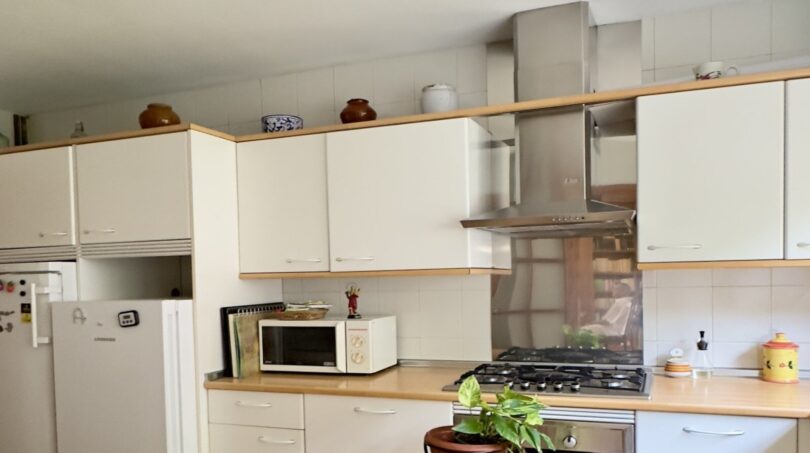 Cocina luminosa con armarios blancos, estufa de gas, campana extractora y refrigerador en la casa adosada Palma de Mallorca.
