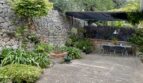 Patio interior bien cuidado con muro de piedra natural, vegetación exuberante y área de comedor cubierta al aire libre
