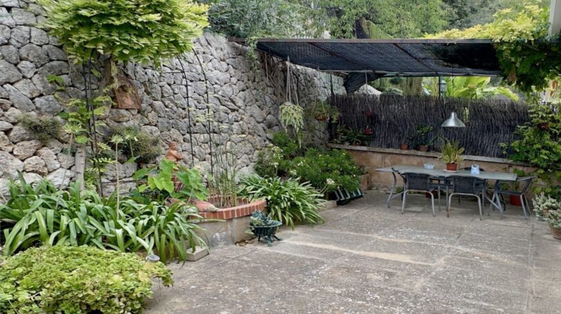 Patio interior bien cuidado con muro de piedra natural, vegetación exuberante y área de comedor cubierta al aire libre