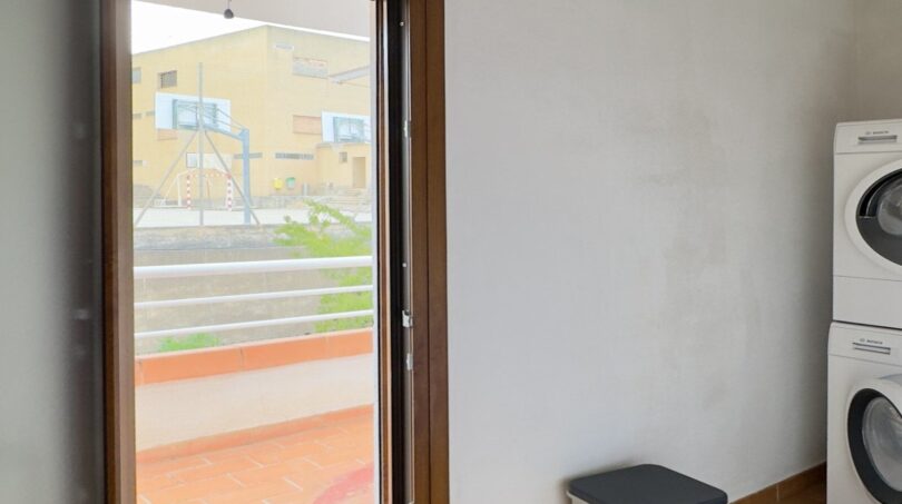 Lavandería con lavadora Bosch apilada, acceso a terraza y vista a las instalaciones deportivas en Palma de Mallorca.