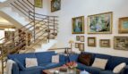 Sala de estar luminosa con sofás azules, mesa de cristal, galería de cuadros y elegante escalera de caracol en la casa adosada de Palma