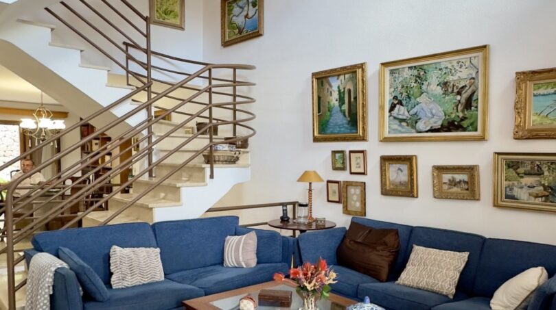 Sala de estar luminosa con sofás azules, mesa de cristal, galería de cuadros y elegante escalera de caracol en la casa adosada de Palma