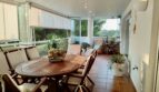 Glazed south-facing terrace with wooden table, chairs and plants, view into nature reserve, apartment Llucmajor