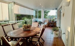 Glazed south-facing terrace with wooden table, chairs and plants, view into nature reserve, apartment Llucmajor