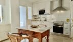 Bright kitchen of the Mallorca apartment with white cabinets, stainless steel hood and rustic wooden table with wicker chairs.