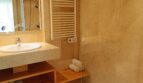 Bright bathroom with marble tiles, shower, towel heater and wooden shelf in Mallorca apartment
