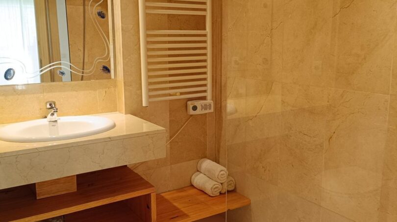 Bright bathroom with marble tiles, shower, towel heater and wooden shelf in Mallorca apartment