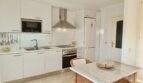 Bright built-in kitchen with white fronts, stainless steel range hood, oven and rustic marble dining table in Mallorca apartment.