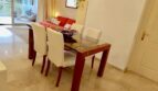 Bright dining room with glass table, white chairs and red sofa in Mallorca apartment in Llucmajor.