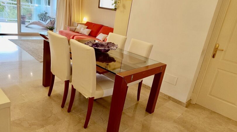 Bright dining room with glass table, white chairs and red sofa in Mallorca apartment in Llucmajor.