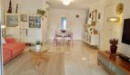 Bright living room with marble floor, orange sofa, glass table and dining area in Mallorca apartment.