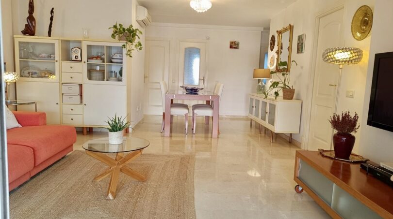 Bright living room with marble floor, orange sofa, glass table and dining area in Mallorca apartment.