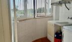 Utility room with washing machine, sink, gas heating and barred windows with green view in Llucmajor.