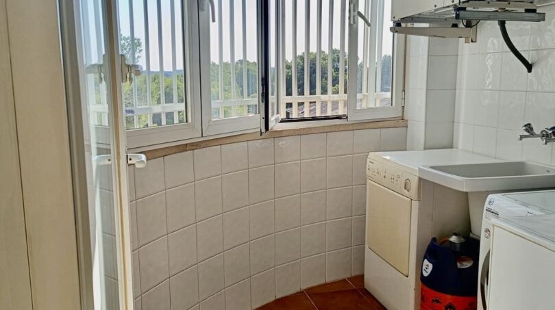Utility room with washing machine, sink, gas heating and barred windows with green view in Llucmajor.