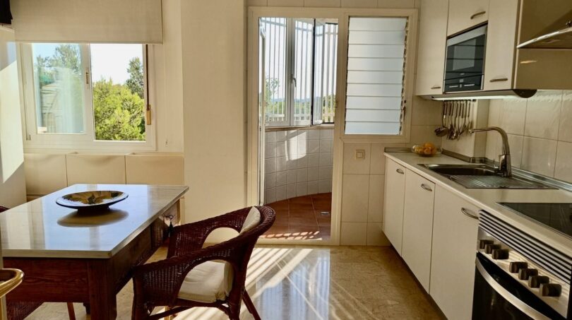 Bright kitchen with dining area, white built-in cabinets and access to the terrace with nature view in Mallorca.