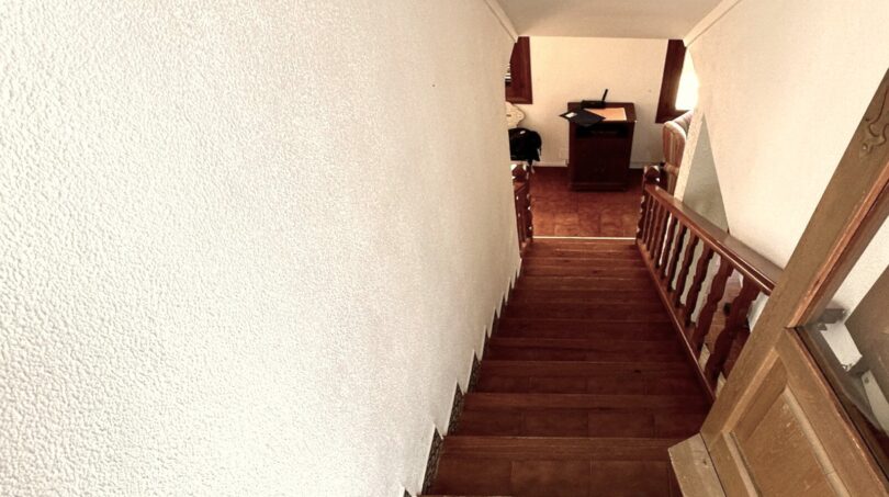 Holztreppe mit Geländer führt in Wohnbereich des Chalets in Palmanyola, helle Wände, rustikales Ambiente.
