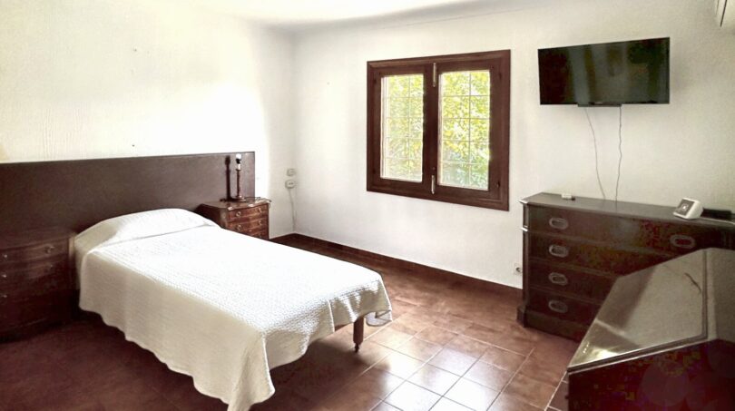 Schlafzimmer des Chalets in Palmanyola mit Einzelbett, Holzmöbeln, Terrakottaboden und Fenster zum Garten.