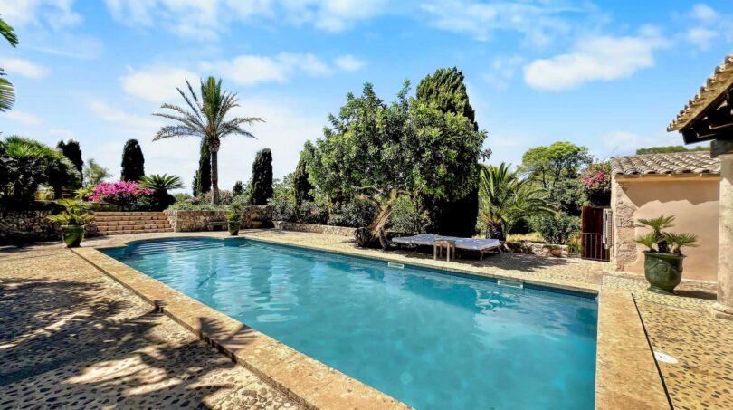 Piscina exterior de la Finca en Felanitx con jardín mediterráneo, palmeras y buganvilia bajo cielo azul