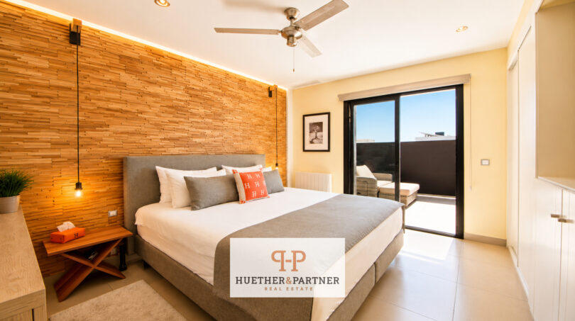 Modernes Schlafzimmer der Luxusvilla in Cala Murada mit Holzwandverkleidung, Deckenventilator und Balkonzugang.