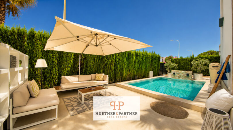 Sonnige Poolterrasse der Luxusvilla in Cala Murada mit eleganter Lounge, Sonnenschirm und Hecke.