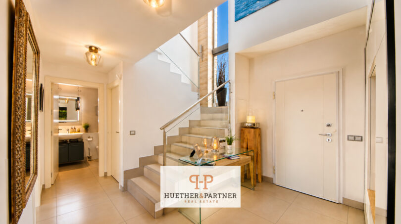 Heller Eingangsbereich der Luxusvilla in Cala Murada mit moderner Treppe, Glasgeländer und elegantem Fliesenboden.