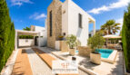 Außenansicht der Luxus-Bauhausvilla in Cala Murada mit Pool, Natursteinturm, weißer Fassade und gepflegtem Garten.