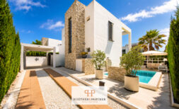 Außenansicht der Luxus-Bauhausvilla in Cala Murada mit Pool, Natursteinturm, weißer Fassade und gepflegtem Garten.
