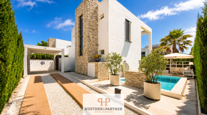 Außenansicht der Luxus-Bauhausvilla in Cala Murada mit Pool, Natursteinturm, weißer Fassade und gepflegtem Garten.
