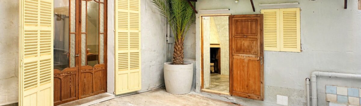 Innenhof der Stadthauswohnung in Manacor mit Holztüren, gelben Fensterläden und Palme im Topf