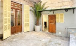 Courtyard of the city house apartment in Manacor with wooden doors, yellow shutters and potted palm tree