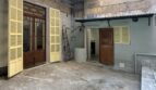 Innenhof des Stadthauses in Manacor mit gelben Holzfensterläden, Betonboden und Holztüren, renovierungsbedürftig.