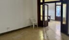 Leerer Wohnraum mit Sechseck-Fliesenboden und Holztür zum Patio, renovierungsbedürftig