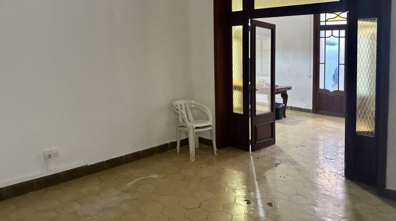 Leerer Wohnraum mit Sechseck-Fliesenboden und Holztür zum Patio, renovierungsbedürftig