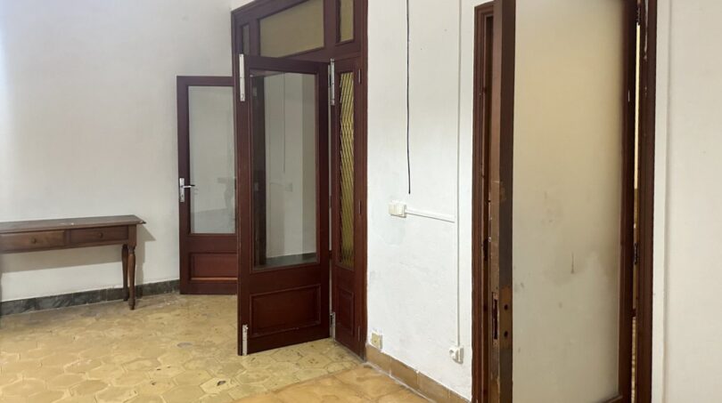 Leerer Durchgangsraum mit dunklen Holztüren und Glasfenstern, Terrakottaboden, renovierungsbedürftig