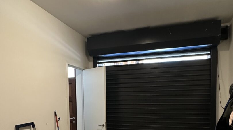 Garage mit schwarzem Rolltor, Seiteneingang, Fluoreszenzlicht und Betonboden im Stadthaus Artà
