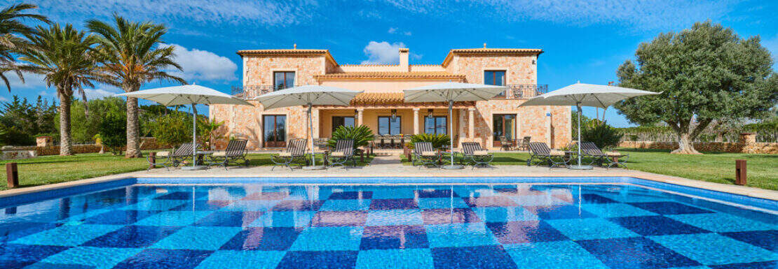 Außenansicht Traum-Finca Mallorca mit großem Schachbrettmuster-Pool, Sonnenliegen und mediterranem Landhaus