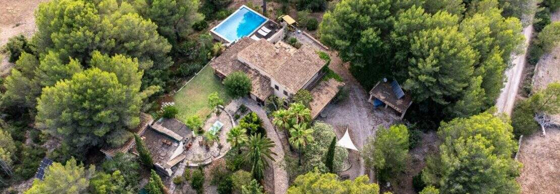 Luftaufnahme einer Natursteinfinca bei Artà mit Pool, Gästehaus und Garten, umgeben von dichtem Pinienwald.