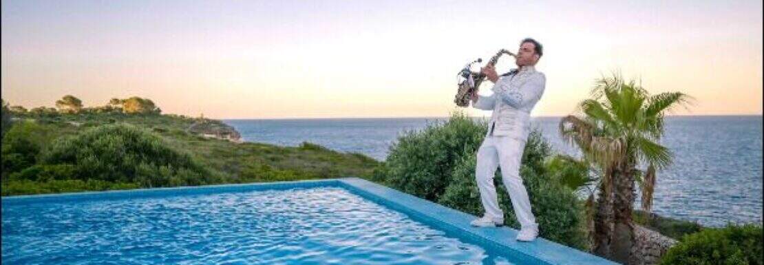 Infinity-Pool mit Meerblick bei Sonnenuntergang, Saxophonist in Weiß, Palmen, Luxusvilla Cala Magrana