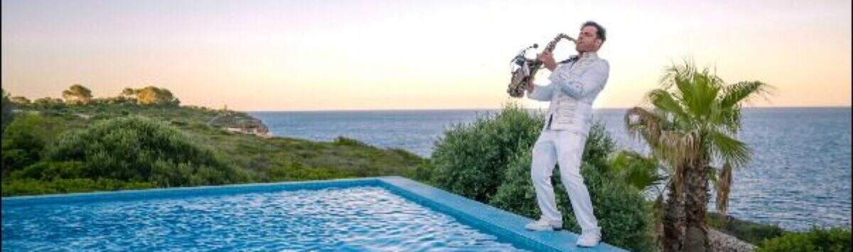 Piscina infinita con vista al mar al atardecer, saxofonista en blanco, palmeras, villa de lujo Cala Magrana