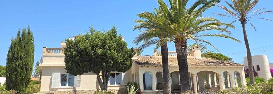 Außenansicht der Villa in Cala Murada mit mediterranem Stil, Palmengarten, Arkaden und Natursteinmauern.