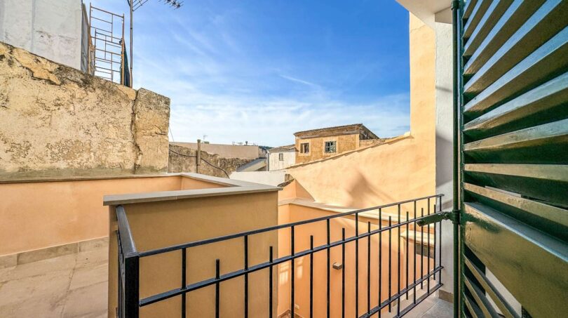 Balkon mit schwarzem Eisengeländer und grünen Holzläden, Blick auf Dächer in Felanitx