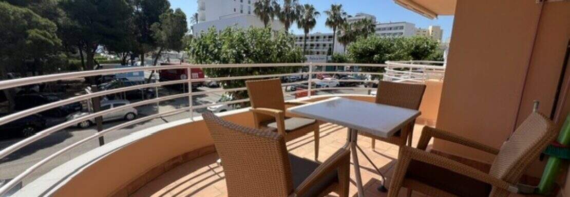 Sonniger Balkon der Wohnung in Cala Millor mit Rattanmöbeln, Rundumgeländer und Blick auf Palmen und Umgebung.