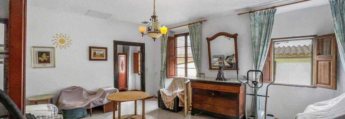 Living room with a chandelier, wooden dresser, mirror, and green curtains in a house in Felanitx