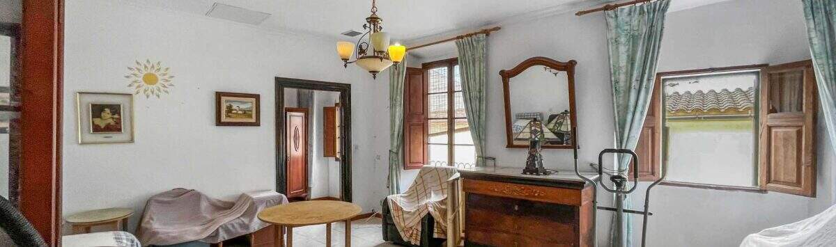 Living room with a chandelier, wooden dresser, mirror, and green curtains in a house in Felanitx