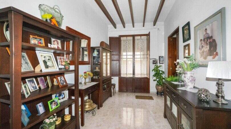 Entrance area with wooden shelves full of family photos, a wooden beam ceiling, and a rustic front door in Felanitx.