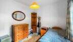 Bedroom with a wooden dresser, mirror, corner shelf, and double bed with a blue bedspread in a house in Felanitx.